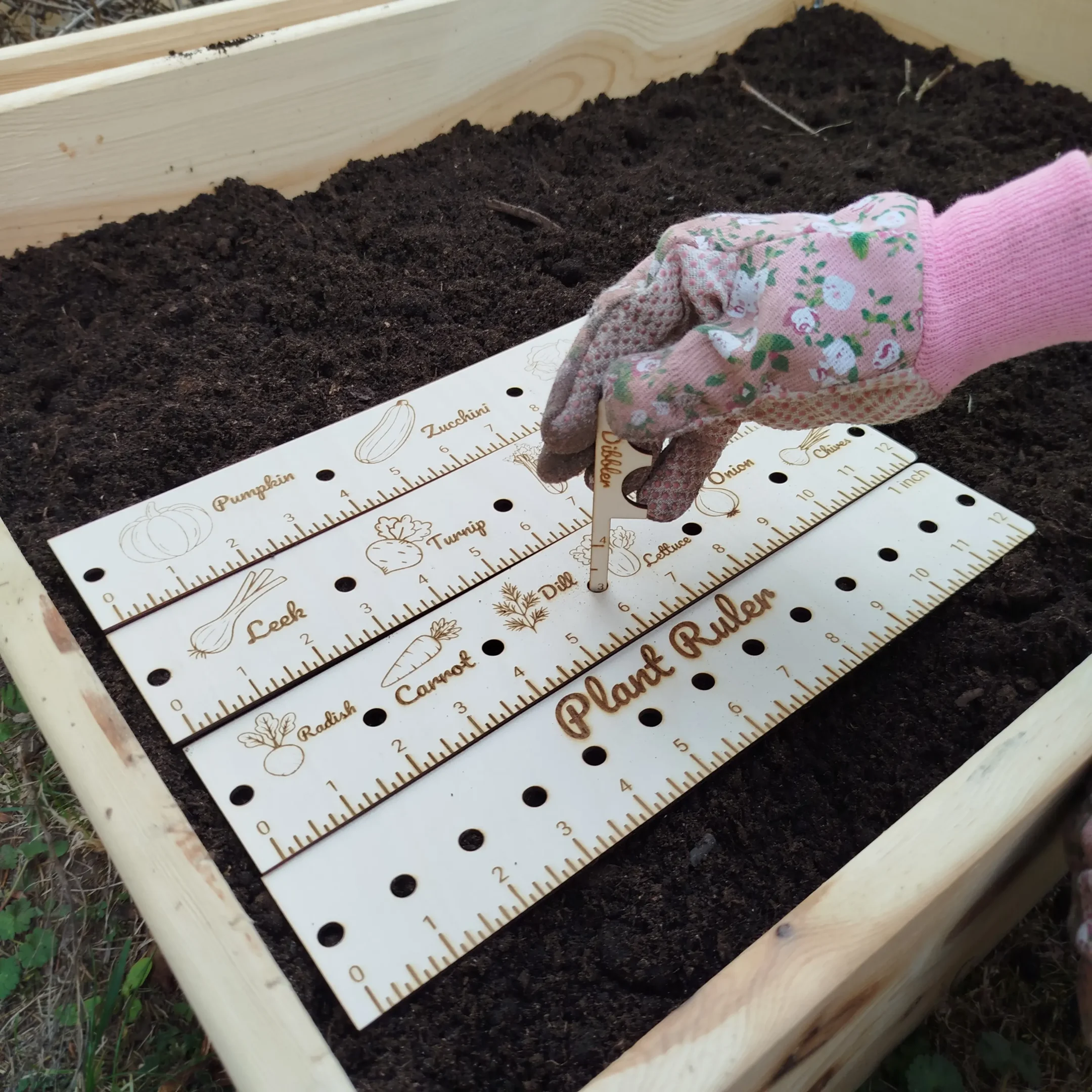 Person holding a laser cut garden dibbler while planting in soil, wearing gardening gloves