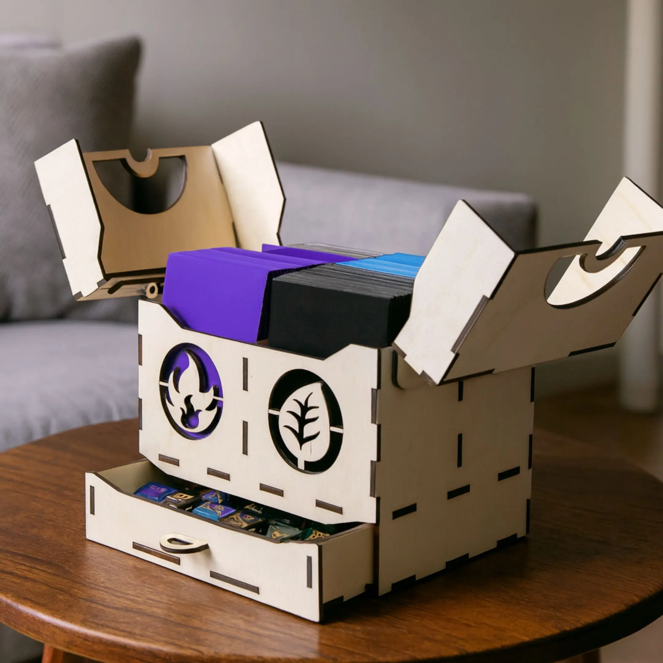 Laser cut wooden trading card deck box with open lids and dice drawer on a table in a room