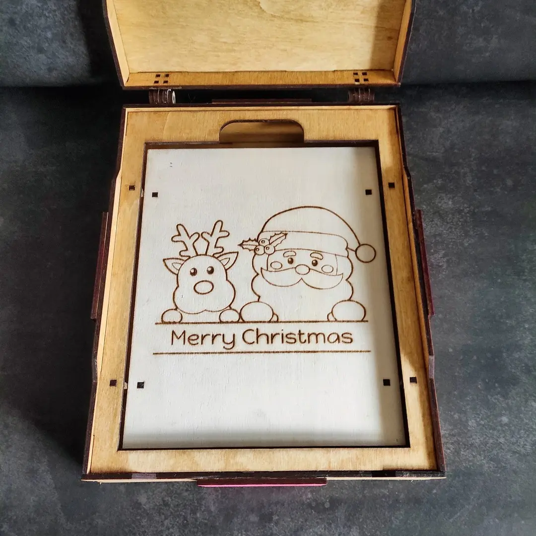 Open laser cut Christmas game gift box with engraved Santa Claus and reindeer inside the lid, empty interior.